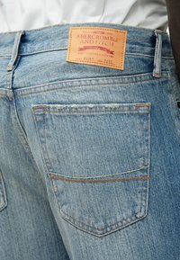 Φωτεινό γαλάζιο τζιν υφάσματος denim με δερμάτινη ετικέτα που φέρει την επιγραφή «Abercrombie and Fitch». Ορατή ραφή, δύο πίσω τσέπες και ελαφρώς ξεθωριασμένη υφή.