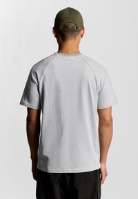 T-shirt grigia a maniche corte con scollo rotondo, maniche raglan, realizzata in tessuto misto cotone, indossata con un cappellino verde dotato di cinturino sul retro.