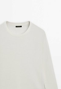 Maglione leggero a maniche lunghe di colore bianco, con scollo rotondo e una fine trama a coste. Etichetta visibile all'uscita dello scollo.