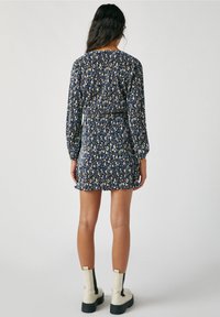 Mekko, jossa on kukkakuosi, tummansininen, pitkät hihat, vyötärö on kiristetty ja helma levenee. Yhdistetty valkoisiin nilkkureihin ja mustiin yksityiskohtiin.