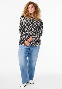 Haut à manches longues noir et crème à motif, associé à un jean large bleu clair et des chaussures blanches, avec une coupe décontractée et un col rond.