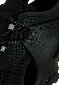 Calzature Crocs nere con esterno testurizzato, pannelli in mesh, lacci elastici e suola in gomma con fori per il drenaggio.