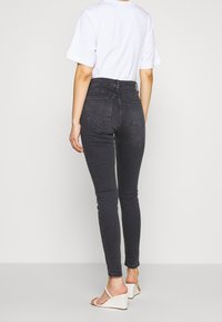 Černé skinny džíny s vysokým pasem, pěti kapsami a hladkým denimovým vzhledem, skombinované s bílým tričkem a světle hnědými wedge sandály.