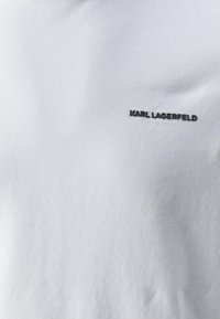 Vit bomullströja med rund halsringning och korta ärmar, med en svart "KARL LAGERFELD"-logotyp på vänster bröst.