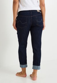Jeans de denim azul oscuro con un diseño de pierna recta, dobladillos enrollados y dos bolsillos traseros que presentan un patrón de olas cosido con hilo de contraste.