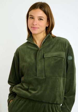 Grüner Cordpullover mit einem halben Reißverschluss-Kragen, Fronttasche und gerippter Textur. Mit einem Logo-Patch am linken Ärmel.