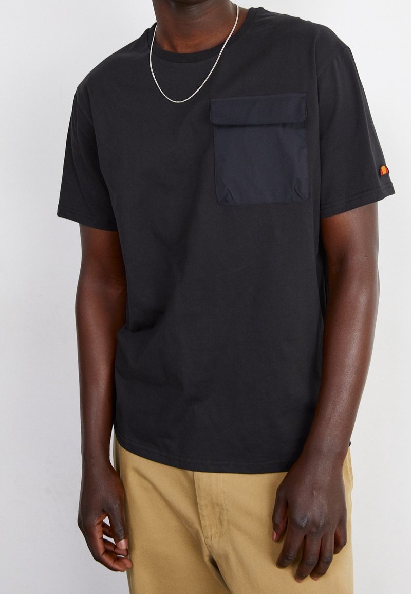 T-shirt en coton noir avec une poche poitrine avant en bleu marine, manches courtes, col rond et un petit accent de logo sur la manche.