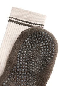 Chaussette côtelée beige avec des rayures foncées associée à une chaussette marron présentant des grips antidérapants en caoutchouc noir sous la semelle.