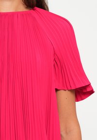 Rosa gefaltetes Kleid mit kurzen, ausgestellten Ärmeln, das einen hohen Halsausschnitt und einen strukturierten Stoff aufweist, der vertikale Linien über das Kleid zieht.