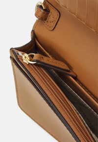 Braunes Lederhandtaschen-Innere mit goldener Hardware, verfügt über ein Reißverschlussfach und unterteilte Bereiche, die ein strukturiertes Design zeigen.