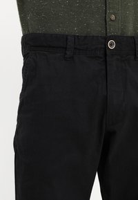 Svarta bomullschinosar med rak passform, med knäppning och bältesloopar. Tyget har en slät textur och minimala sömdetaljer.