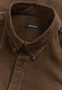Barna kordbársony gombos ing, gombolható gallérral és fekete "Matinique" címkével a nyakrészben.