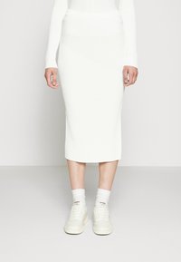 Bílá proužkovaná sukně střední délky s asymetrickým designem. V kombinaci s bílými teniskami a zakrývanými bílými ponožkami. Hladká textura.