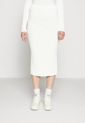 Weiße gerippte Midilänge-Rock mit asymmetrischem Design. Kombiniert mit weißen Sneakern und gekrempelten weißen Socken. Glatte Textur.