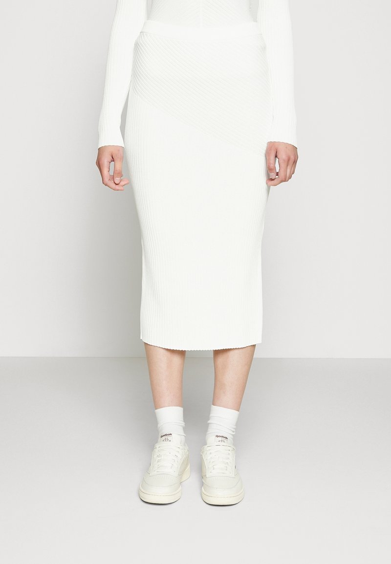 Bílá proužkovaná sukně střední délky s asymetrickým designem. V kombinaci s bílými teniskami a zakrývanými bílými ponožkami. Hladká textura.