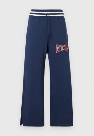 Μπλε ναυτικό φαρδύ παντελόνι φόρμας με λευκή ριγέ ελαστική μέση, κορδόνι, πλευρικές σχισμές και κόκκινο λογότυπο "NIKE" στο αριστερό μηρό.