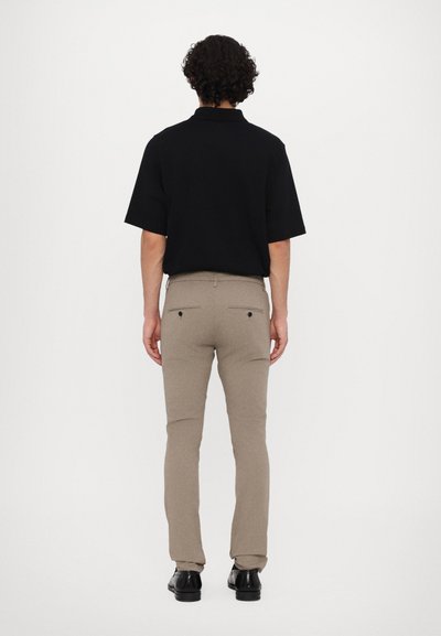 Svart kortärmad polo t-shirt med en avslappnad passform, tillsammans med ljusbeiga slim-fit byxor och svarta läderskor.