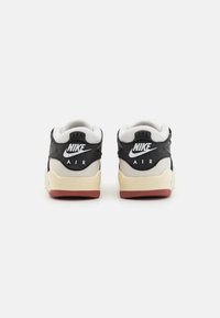 Zapatillas Nike en blanco y negro con una parte superior texturizada, un collar blanco acolchado y una suela crema con acentos rojos en el talón.