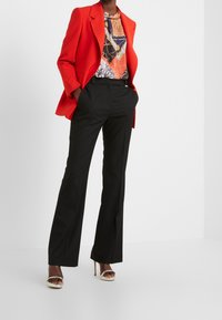 Rode blazer, gebloemd blouse met blauwe, oranje en gouden accenten, zwarte op maat gemaakte broek, en gestrikte hoge hakken sandalen.