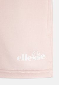 Gai rozā kokvilnas šorti ar gludu tekstūru un sānu kabatām. Apakšējā kreisajā stūrī ir drukāts balts "ellesse" logotips.