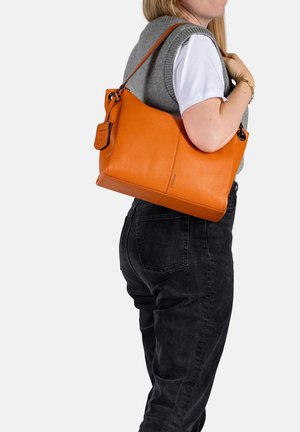 Orange leather handbag with a textured finish, featuring a detachable tag and a contrasting strap, worn on the shoulder against a grey backdrop.