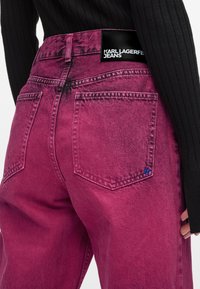 Fuksija traperice s izblijedjelom teksturom, dizajnom s pet džepova i crnom etiketom s natpisom "KARL LAGERFELD JEANS" na struku.