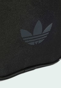 Borsa in tessuto nera con superficie texture, un logo a tre strisce grigio scuro ben visibile e una zip curva.