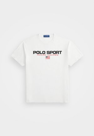 Balts kokvilnas T-krekls ar uzrakstu "POLO SPORT" uzrakstīts treknrakstā melnā krāsā, "RALPH LAUREN" sarkans, un neliela Amerikas karoga grafika zem tā.