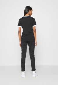 T-shirt preta com colarinho e acabamentos das mangas brancos, combinada com calças pretas com riscas laterais brancas. Usada com sapatilhas brancas.