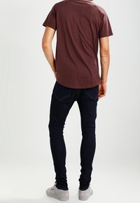Mörkröd kortärmad skjorta i kombination med mörkblå skinny jeans och grå sneakers, vilket visar en minimalistisk design och avslappnad passform.