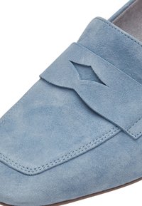 Ljusblå mockaloafers med en sydd söm och en dekorativ utskärning på ovansidan. Slät textur och minimalistisk design.
