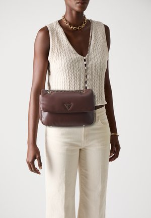 Person wearing cream cable-knit sleeveless top and pants, carrying brown leather shoulder bag with chain strap and gold necklace.