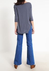 Grå långärmad topp med djup rygg, kombinerad med blå utsvängda jeans och bruna plattformsskor. Outfiten har släta material och en avslappnad passform.