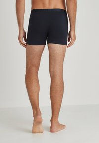 Boxer shorts blu navy con una cintura elastica liscia. Il tessuto sembra aderente e si allunga leggermente, evidenziando le gambe e il torso.