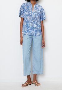 Blusa floreale blu a maniche corte con colletto alla cinese, abbinata a jeans azzurri a gamba larga e sandali piatti beige. Outfit semplice e casual.