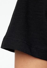 Primo piano di un tessuto nero che mostra una superficie morbida e texturizzata con un orlo piegato. Cuciture ben rifinite visibili lungo il bordo.