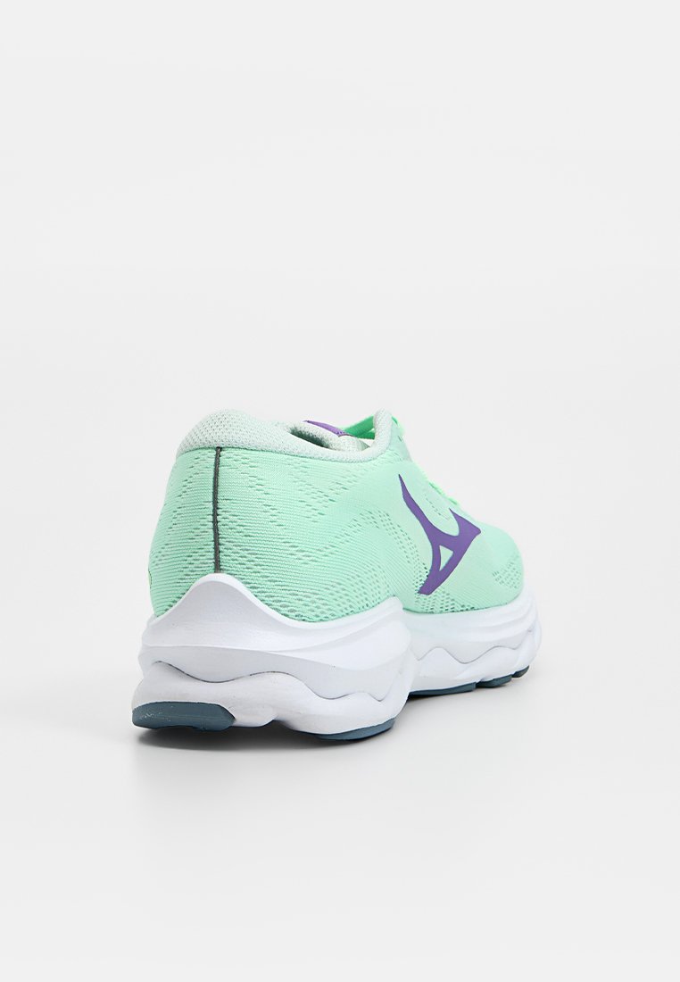 Zapatilla deportiva verde claro con parte superior de tela texturizada, media suela blanca y detalle de logo morado. Diseño de talón redondeado para mayor amortiguación.