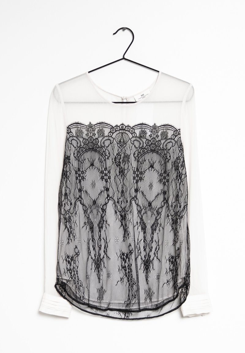 Top en dentelle noire avec des manches longues transparentes, présentant un motif élaboré en dentelle sur un fond clair. Ourlet arrondi avec des détails de pli.