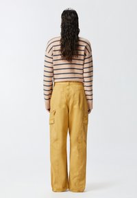 Svijetlopinkasti i mornarski prugasti pulover u kombinaciji s žutim širokim cargo hlačama s bočnim džepovima i ležernim krojem.