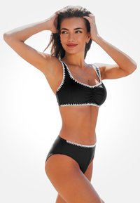 Schwarzer Bikini mit weißem Zickzack-Dekor, bestehend aus einem taillierten Oberteil mit Raffung und hochgeschnittenen Bottoms. Glatte Textur, modernes Design.