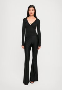 Black long-sleeve top with a twist detail and gold circular accent, paired with fitted black flared pants, both in a sleek, smooth fabric.