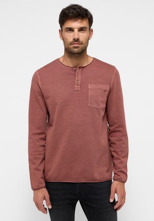 Košeľa s dlhými rukávmi v medenej farbe, s okrúhlym výstrihom, trojbuttonovým zapínaním a náprsníkou na ľavej strane; vyrobená z mäkkej látky s jemnou textúrou.
