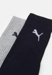 Mustriga mustad ja hallid sokid, millel igas sokis on valge Puma logo. Must sokk on paksem ja tumedam, samas kui hall sokk on heledam ja tekstureeritud.