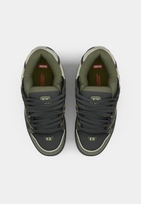 Black and olive green sneakers with round toe, textured upper, yellow eyelets, and cushioned insole. Features logo on the tongue and side.