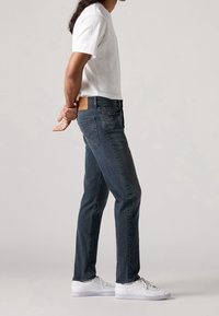 Mörkblå denimjeans med rak passform, läderbakpatch och sidofickor. Bärs med en enkel vit t-shirt och vita sneakers.