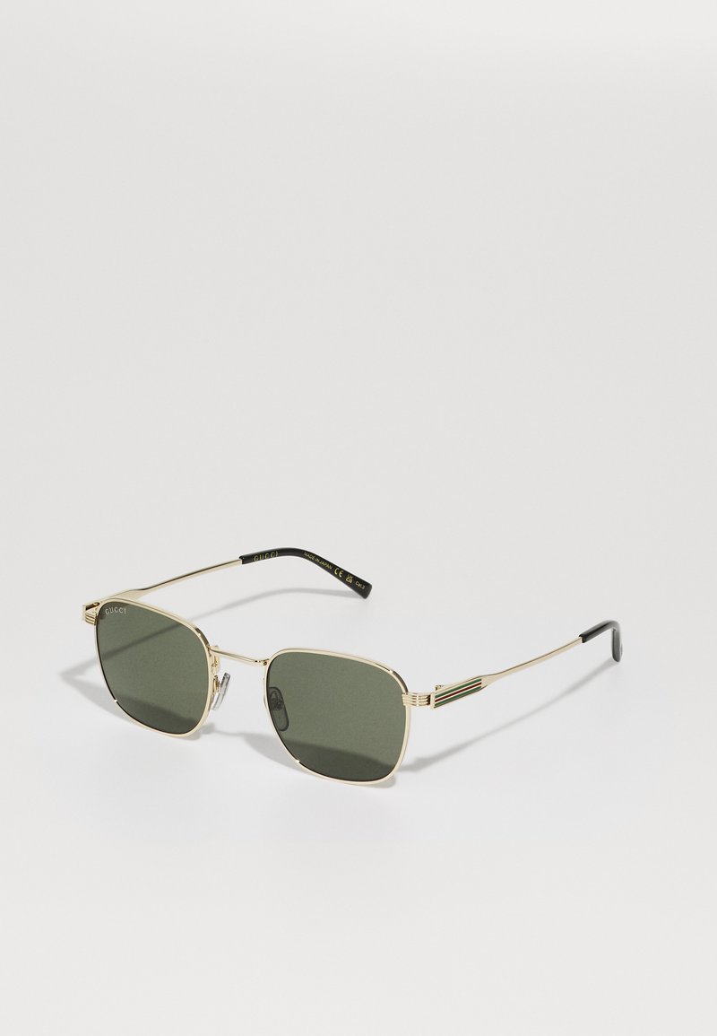 Gafas de sol cuadradas de metal dorado con lentes verde oscuro. Cuentan con patas delgadas y extremos con acentos en negro, adornadas con un detalle del logo en el marco.