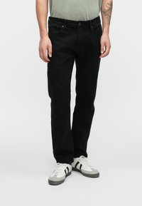 Vaqueros de mezclilla negra con un corte recto, que cuentan con un diseño clásico de cinco bolsillos y una cintura con botones, combinados con zapatillas gris y blancas.