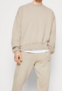 Beige sweatshirt med rund halsringning, lös passform och synliga söm detaljer. Matchat med beiga sweatshirtbyxor med logotyp-accenter.