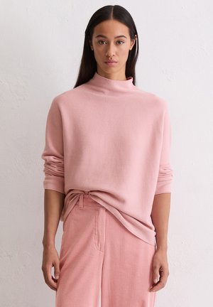 Roze gebreide trui met een hoge hals, relaxte pasvorm en omgeslagen mouwen, gecombineerd met bijpassende geribde ribfluwelen broek. Soepele textuur.