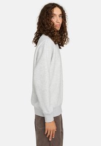 Sudadera gris de cuello redondo con puños y dobladillo acanalados, hecha de una tela suave y texturizada. Diseñada con un corte relajado y un diseño minimalista.